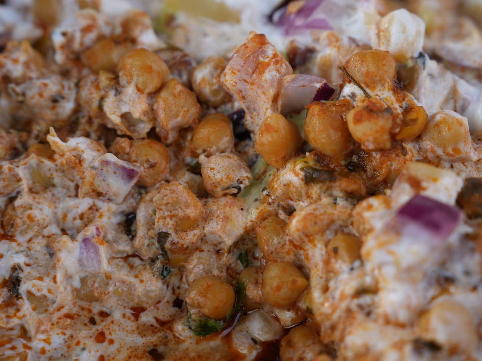 A close-up of chana chaat: chickpeas dressed with yoghurt, red onion and coriander.